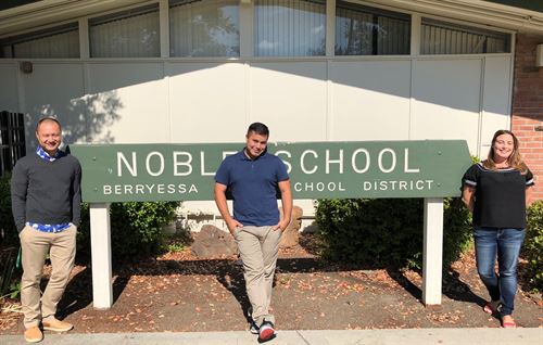 Three fifth grade staff members standing in front of a green Noble School sign